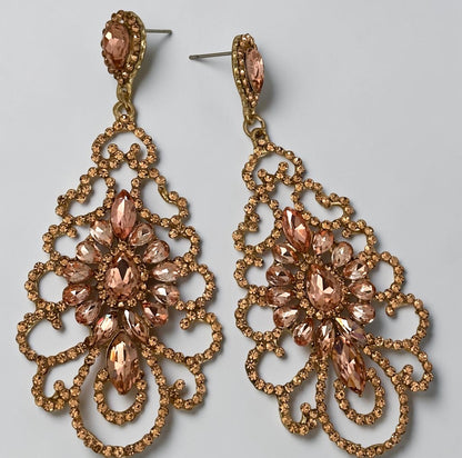 A pair of ornate gold-tone drop earrings with peach-pink faceted rhinestones, displayed on a light gray background.