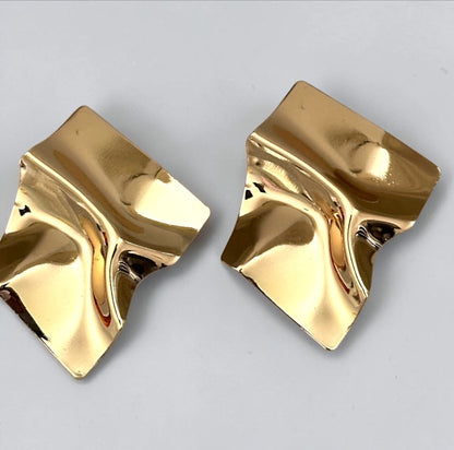 Oversized gold-tone sculptural metal statement stud earrings with a polished wavy design.