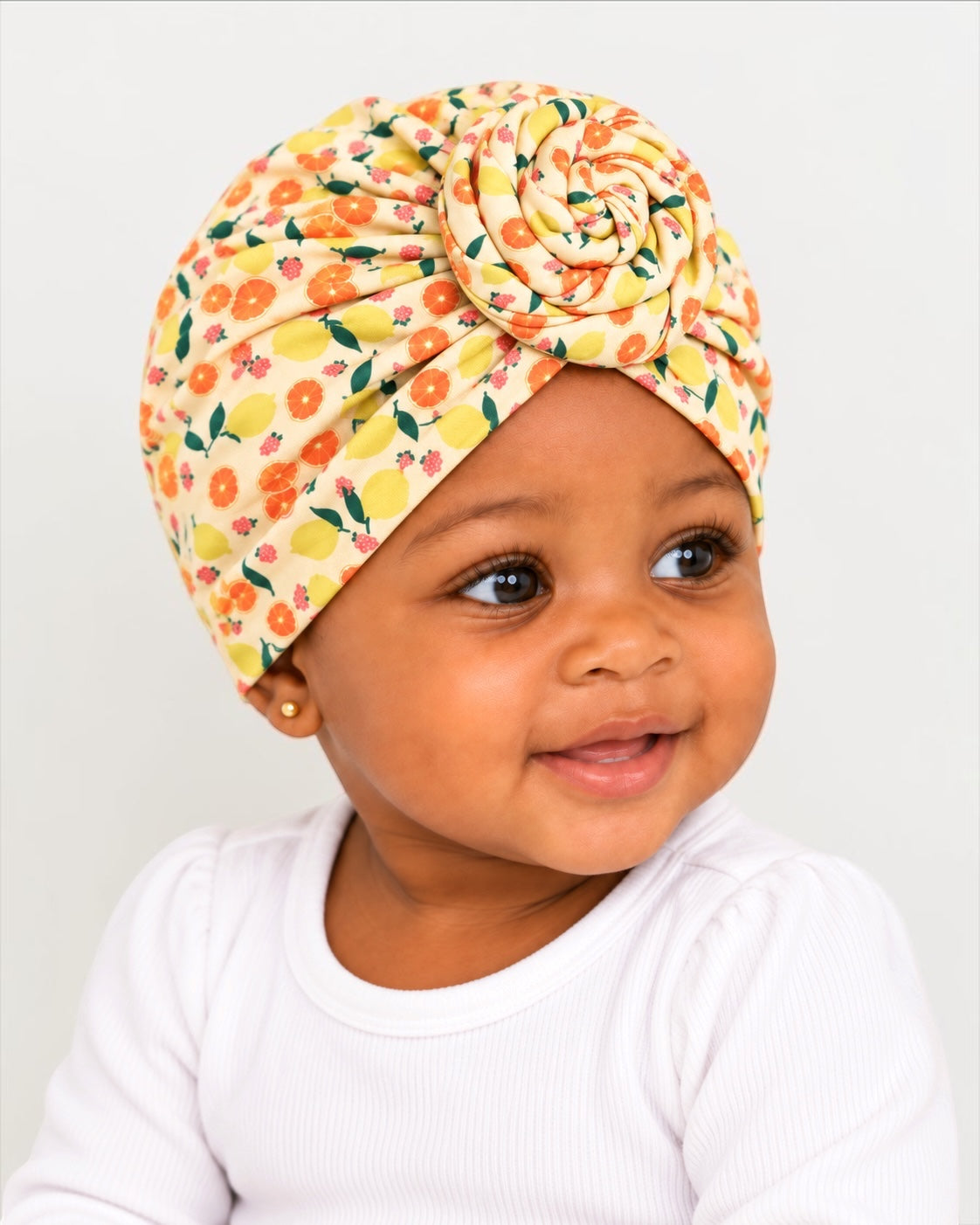 Baby wearing a stretchy jersey fruit print pre-tied turban cap with spiral front knot Fatisha Boutique